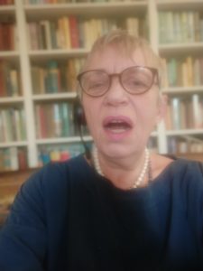 Cllr Caroline Page speaking via zoom: head and shoulders shot in front of bookshelves